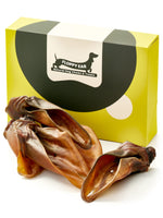 Floppy Ear Beef Ears Chew Box closed with several natural dried beef ears arranged in the foreground