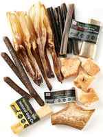 Flat lay of all contents from Floppy Ear Medium Puppy Box – Himalayan yak chews, Scottish Highlands red deer antler, fallow deer antler, beef strips and natural treats on white background