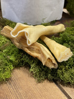 Floppy Ear 100% Natural Air Dried Lamb Skin Dog Chew close up showing rolled texture on moss